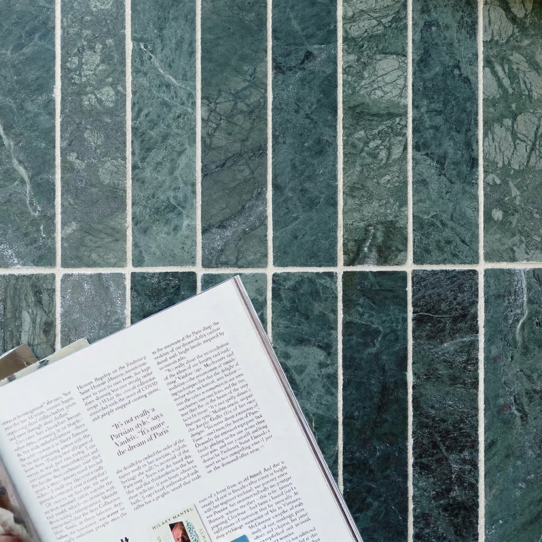 Deep green tumbled stone tiles with natural veining arranged in a grid beneath an open magazine page.