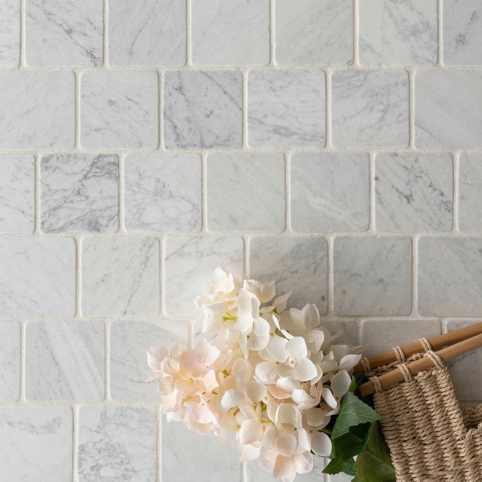 Light gray square marble tiles with natural veining and a soft sheen, arranged behind pale pink hydrangea flowers and woven baskets