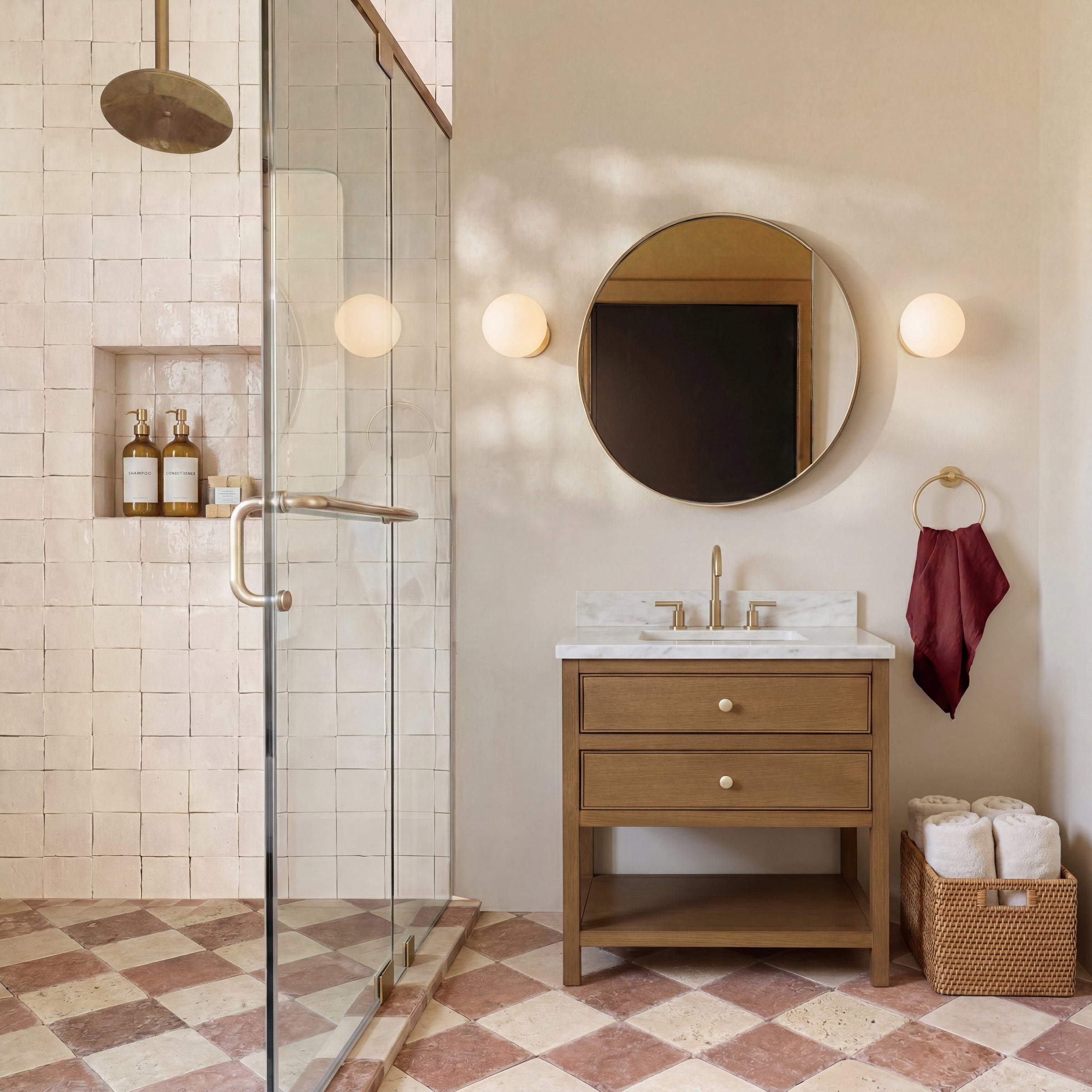 Bathroom with patterned tile floor, oak vanity with marble top, round mirror, wall sconces, glass shower enclosure, and towel basket