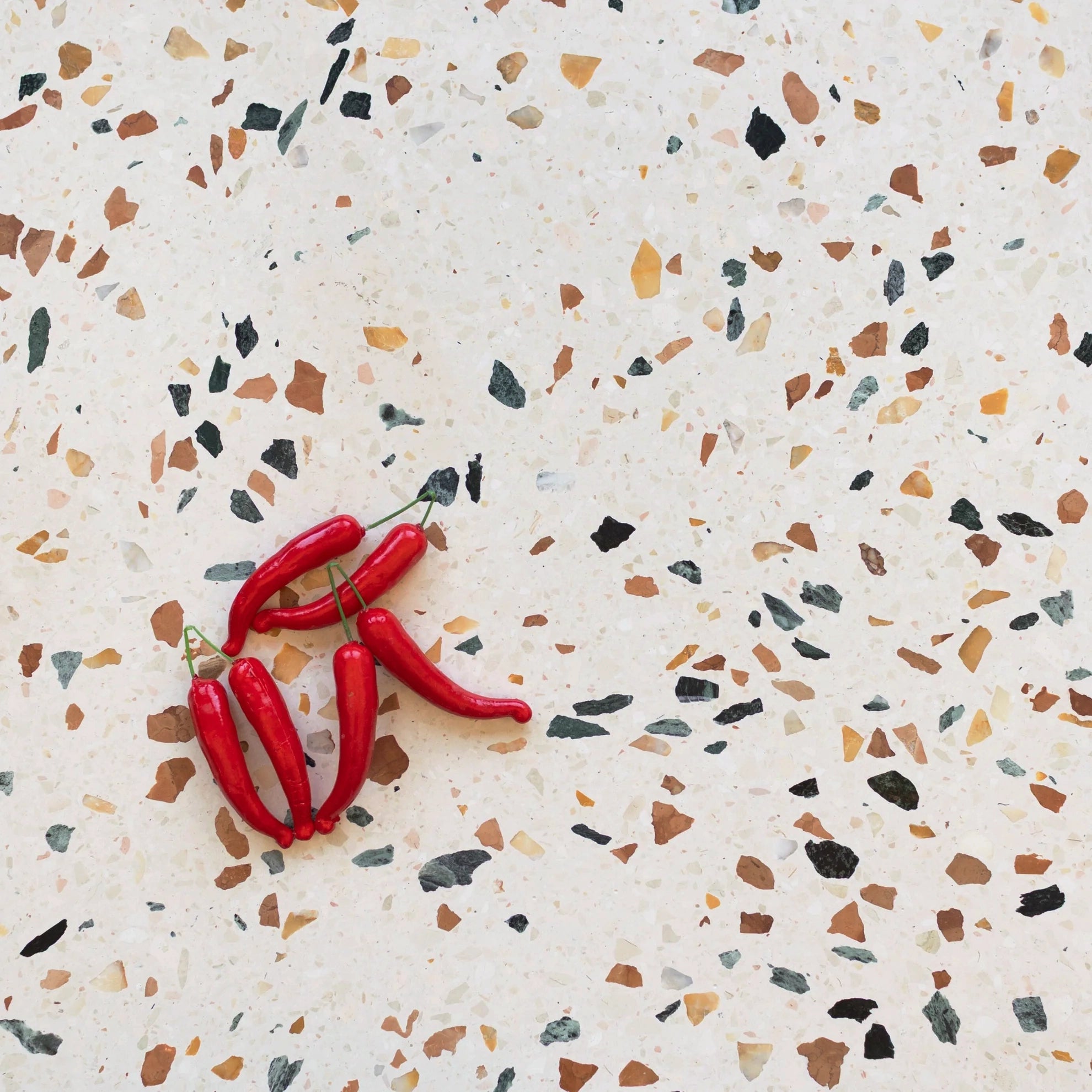 Terrazzo surface with scattered multicolor stone chips and a small cluster of red chili peppers on top