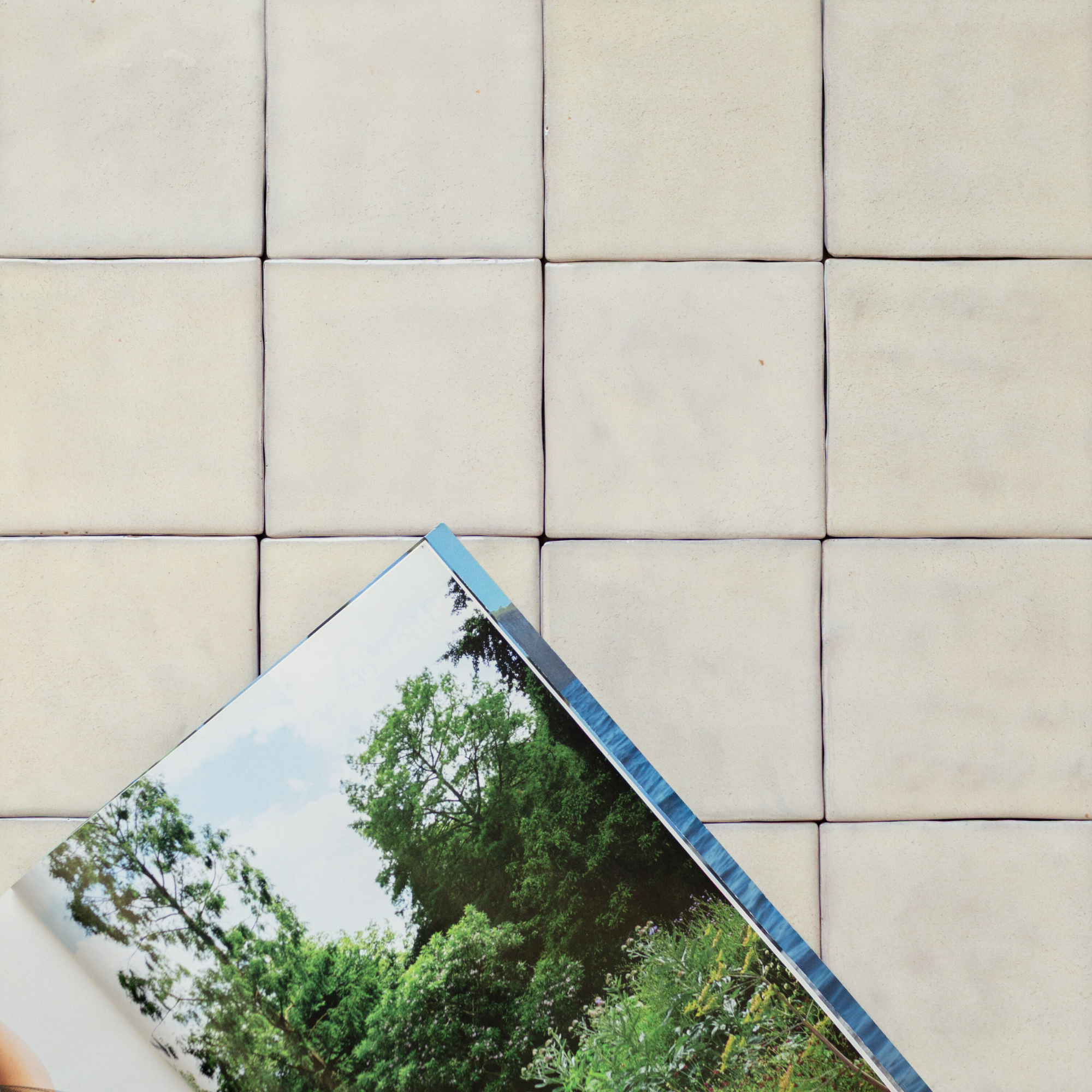 Off-white rustic square ceramic tiles arranged in a grid with an open nature photography book partially visible in the corner