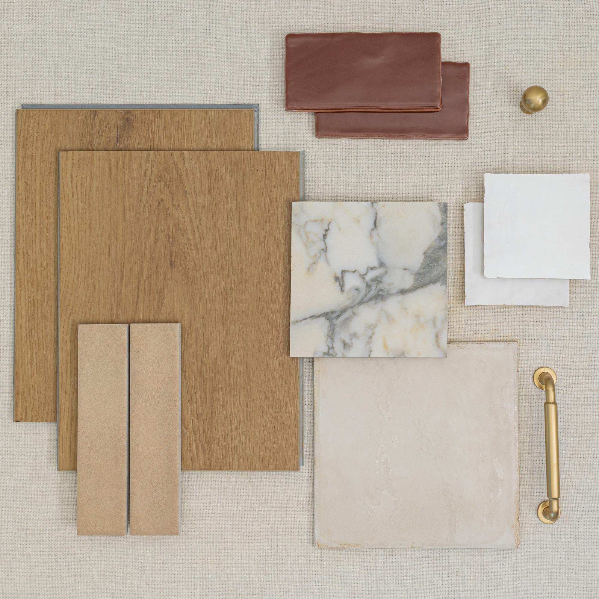 Flat lay of oak wood flooring samples, cream marble and beige ceramic tiles, terracotta and white tile pieces, with brass hardware accents on fabric