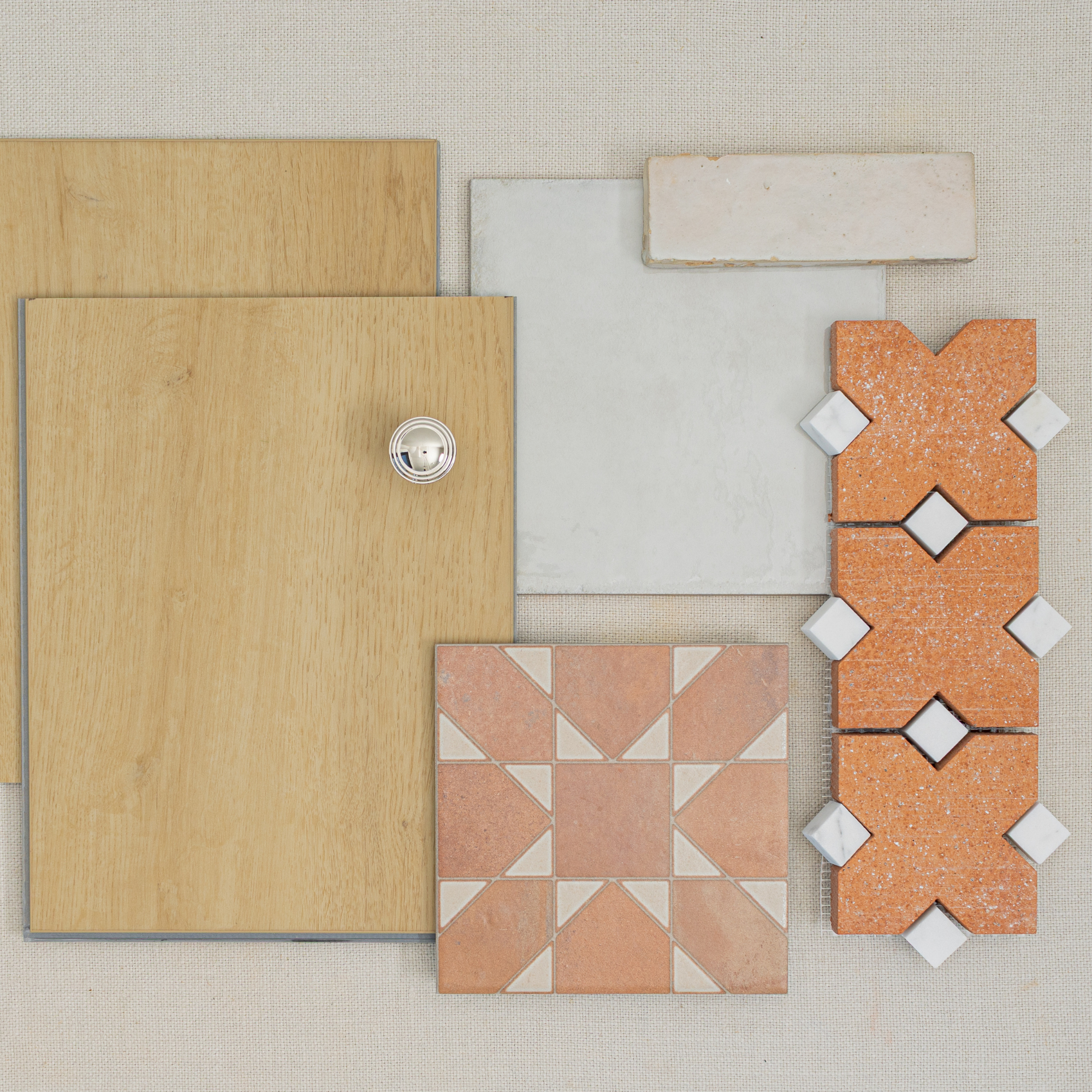 Assorted ceramic and vinyl flooring samples including wood-look planks, terracotta patterned tiles, and textured mosaic pieces arranged on fabric