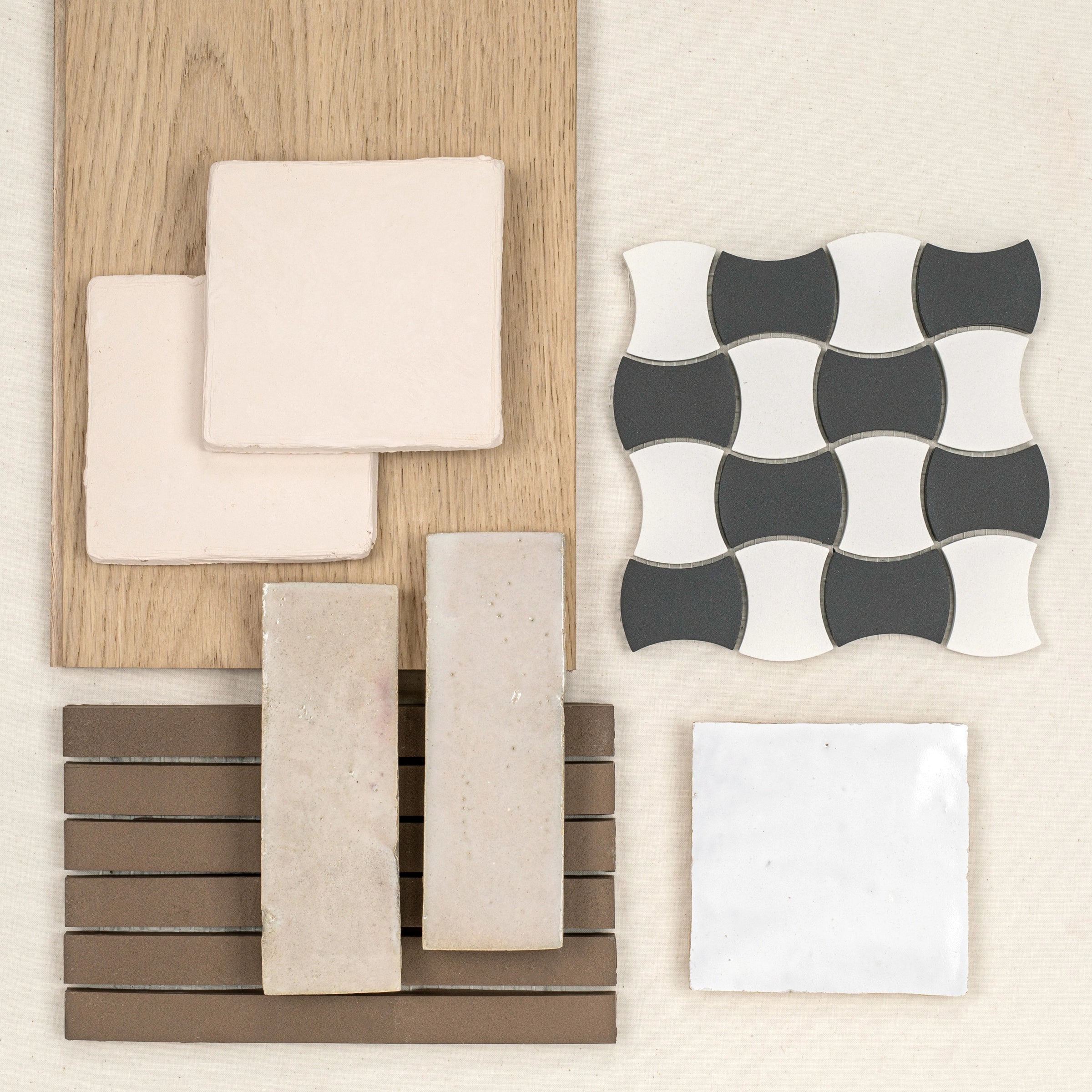 Collection of neutral ceramic tiles arranged with wood samples and a monochrome sculpted tile pattern on light surface