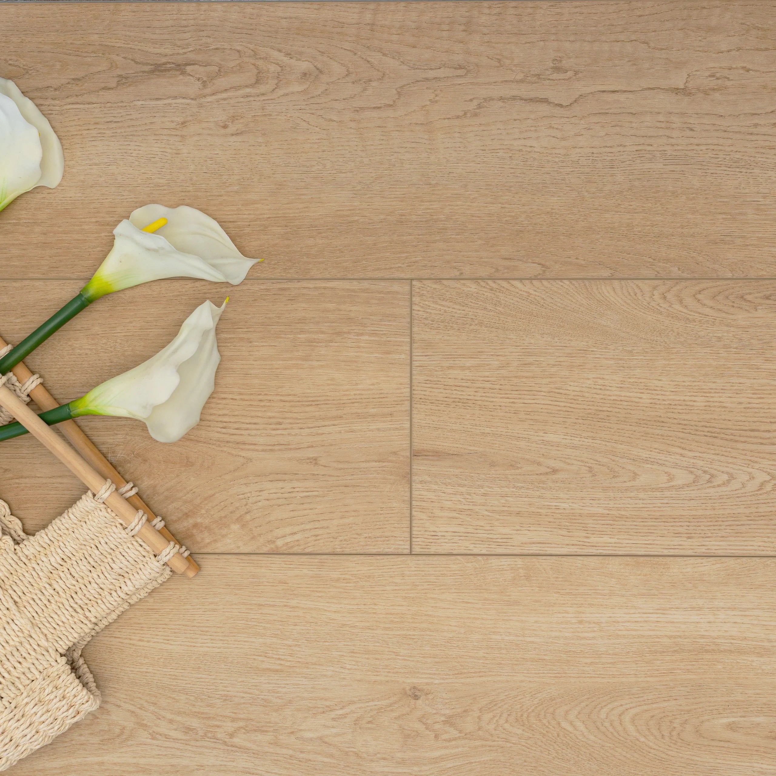 Light wood-look vinyl flooring panels with subtle grain texture, styled with white calla lilies and woven natural fibers.