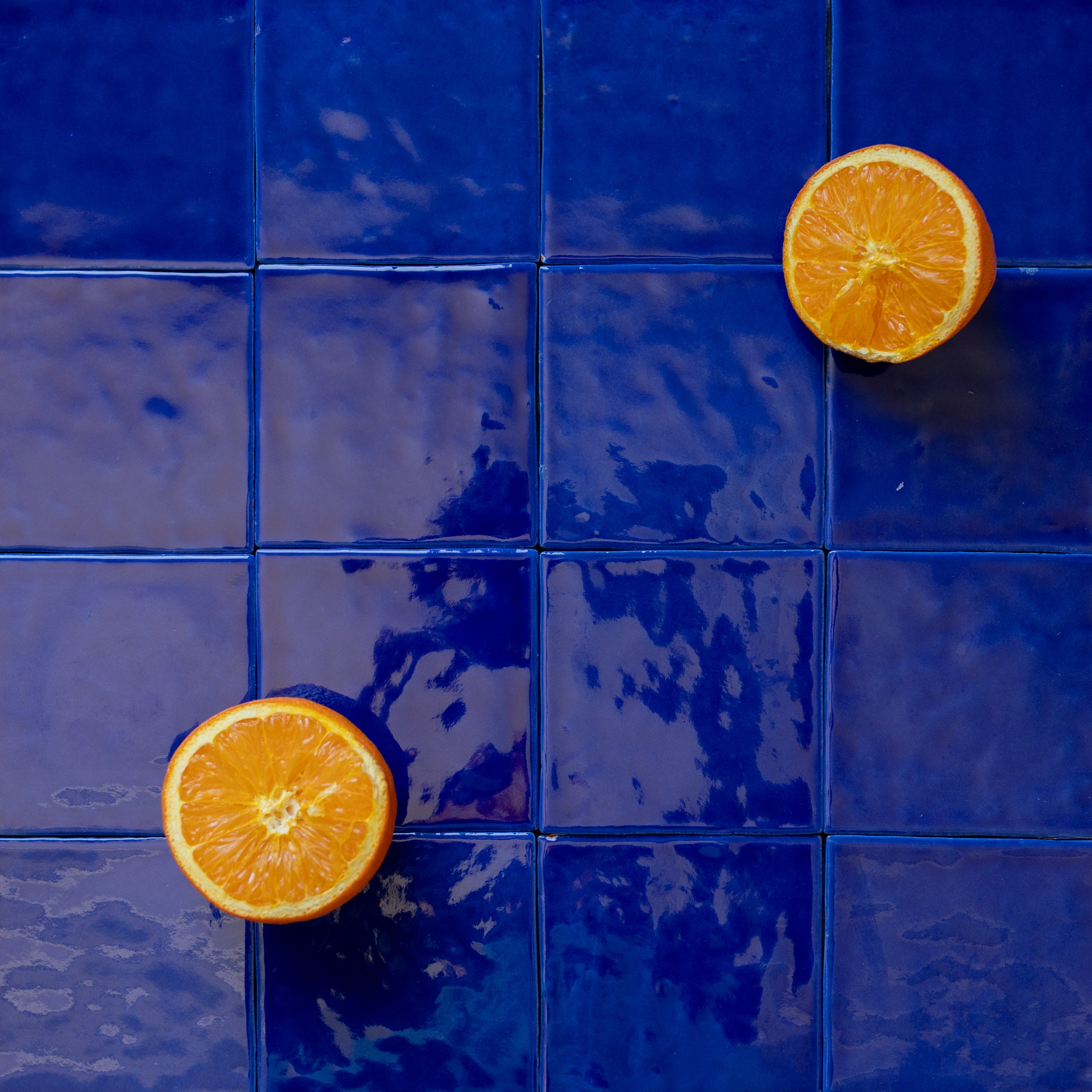 Glossy deep blue ceramic tiles with a subtle texture and two bright orange fruit halves placed on top for contrast