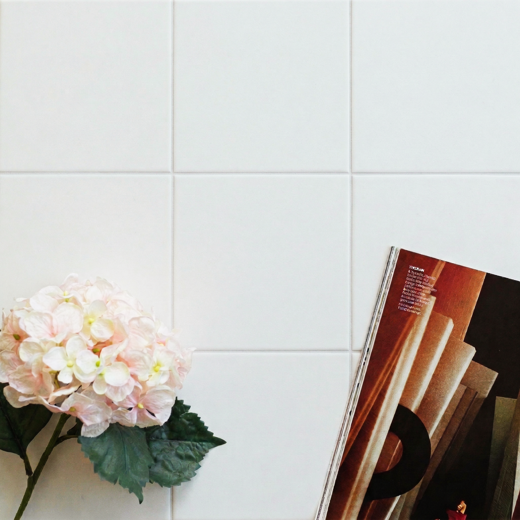 White ceramic tiles arranged in a grid with a pink hydrangea and an open magazine on the side