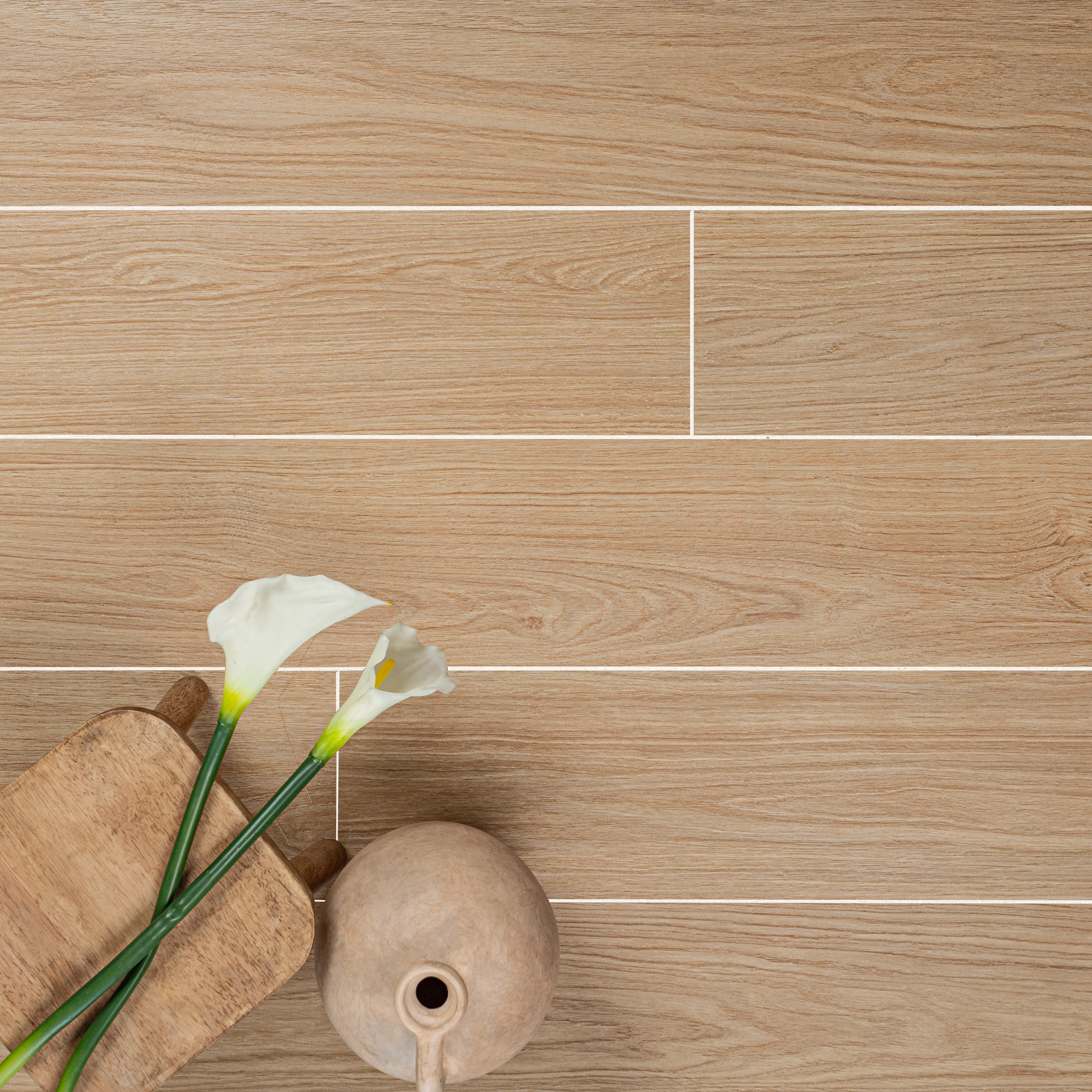 Light honey-toned engineered wood flooring with natural grain texture styled with a wooden tray, vase, and white calla lilies