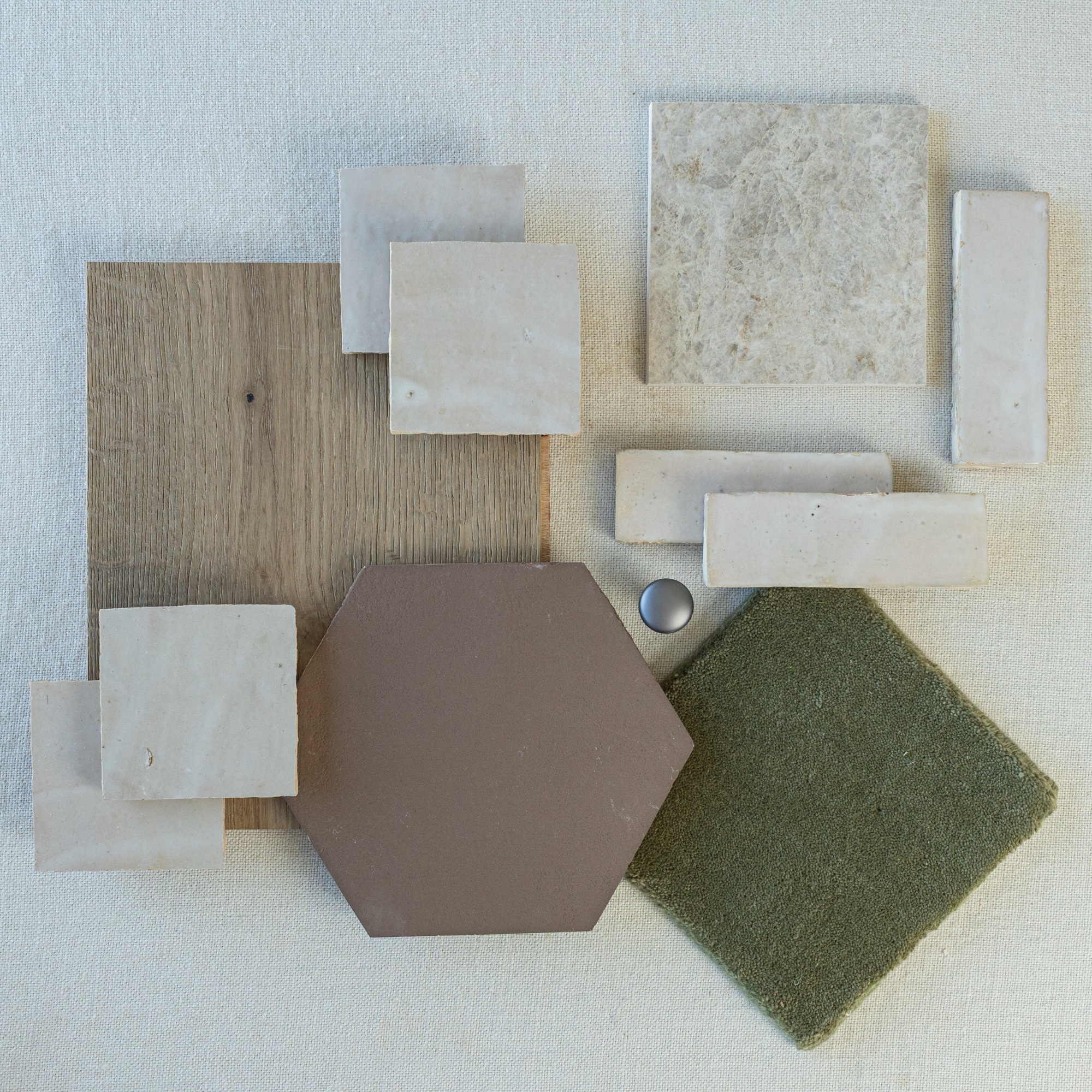 Flat lay showing beige ceramic tiles, green textured tile, brown hexagonal tile, wood plank, and silver hardware on neutral fabric background