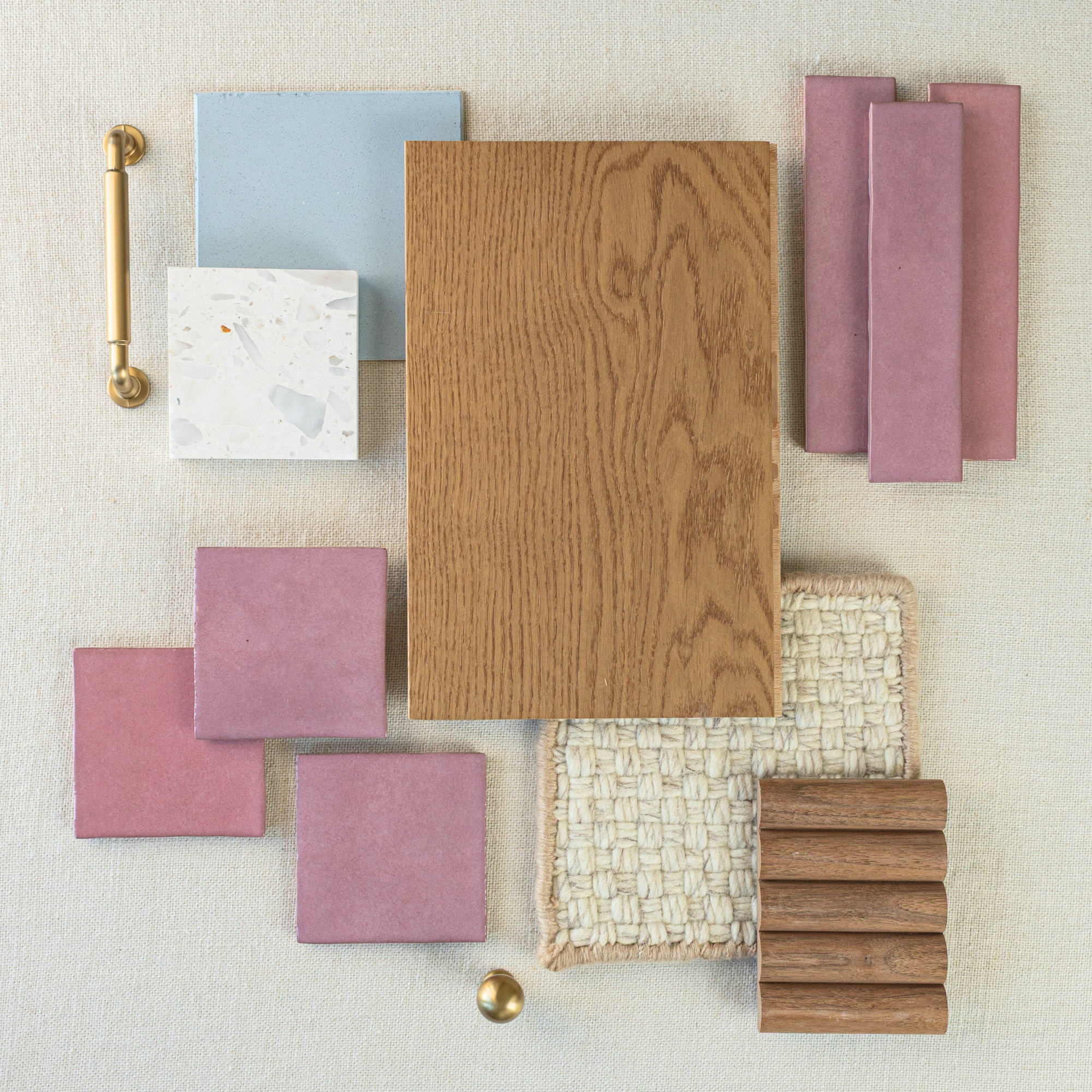 Flat lay of pink and blue ceramic tiles, wood sample, woven fabric swatches, and brass hardware on textured neutral background