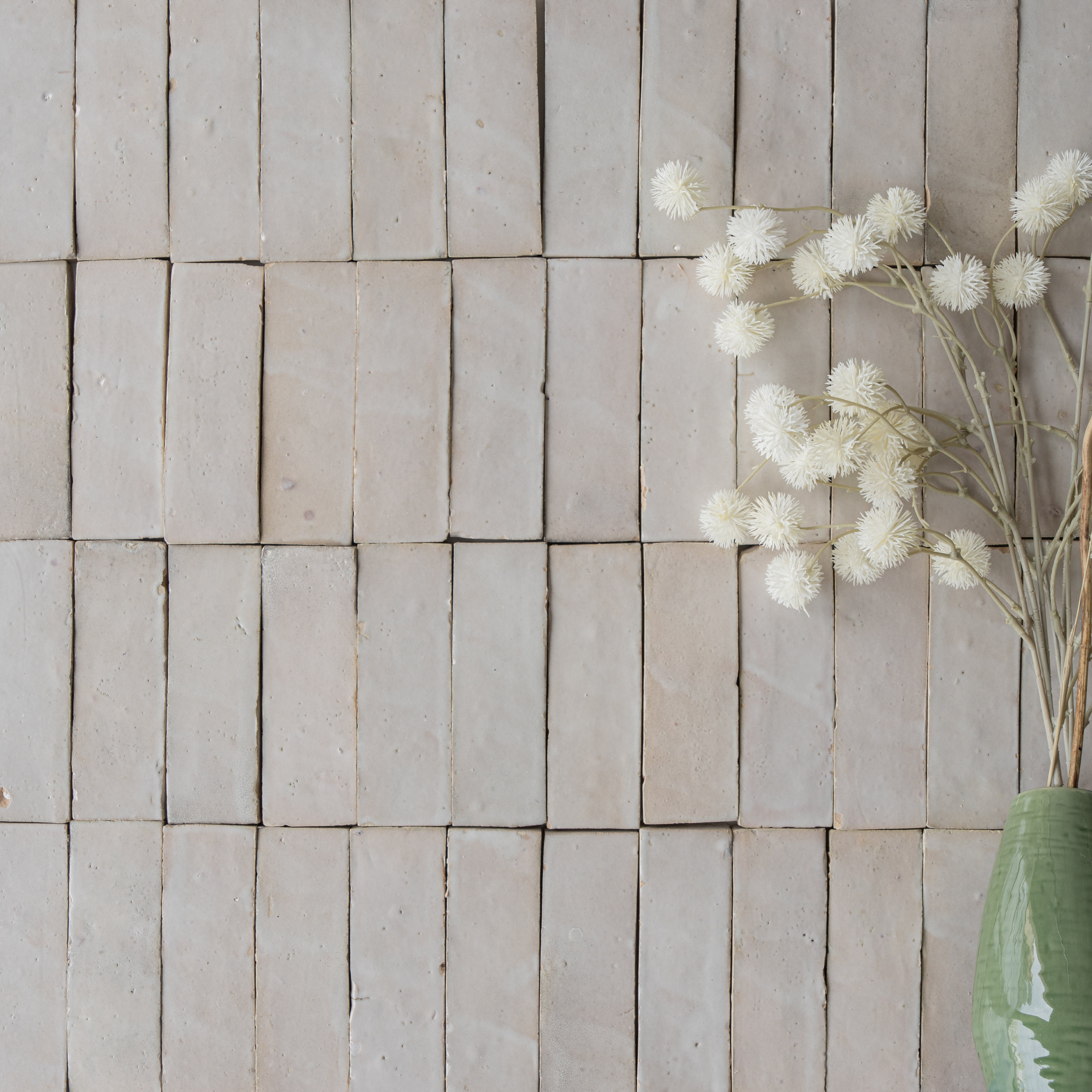 Matte rectangular light beige ceramic tiles arranged in a grid with dried white flowers in a green vase nearby