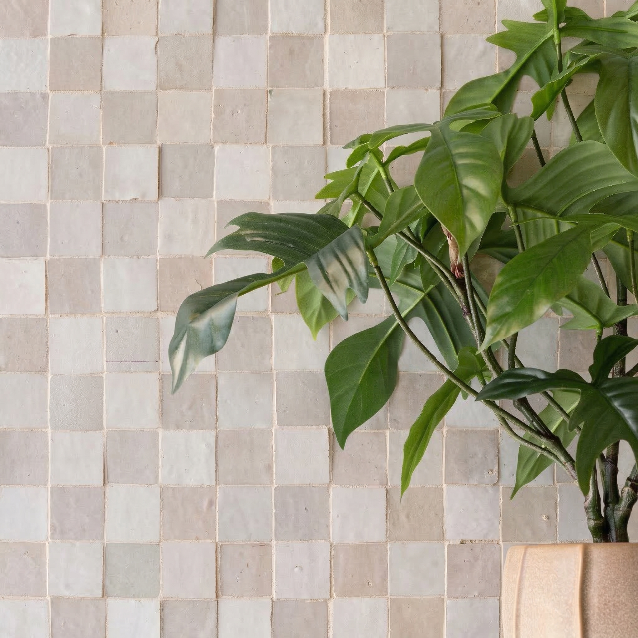 Subtle two-tone beige ceramic tile mosaic with a soft matte finish beside a leafy green plant in a tan planter