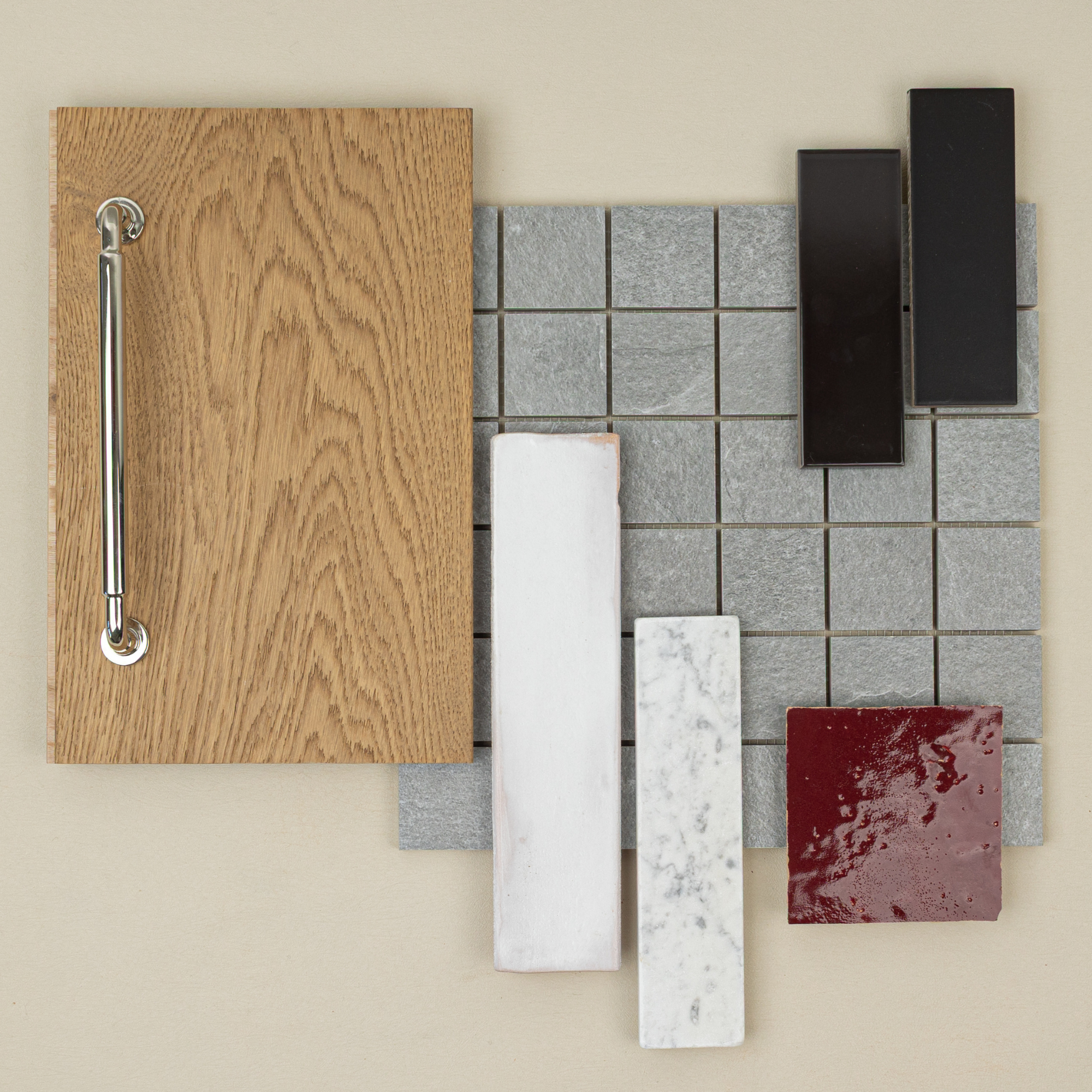 Flat lay of light oak wood sample with small gray slate tiles and white, black, and deep red ceramic tile swatches on neutral surface