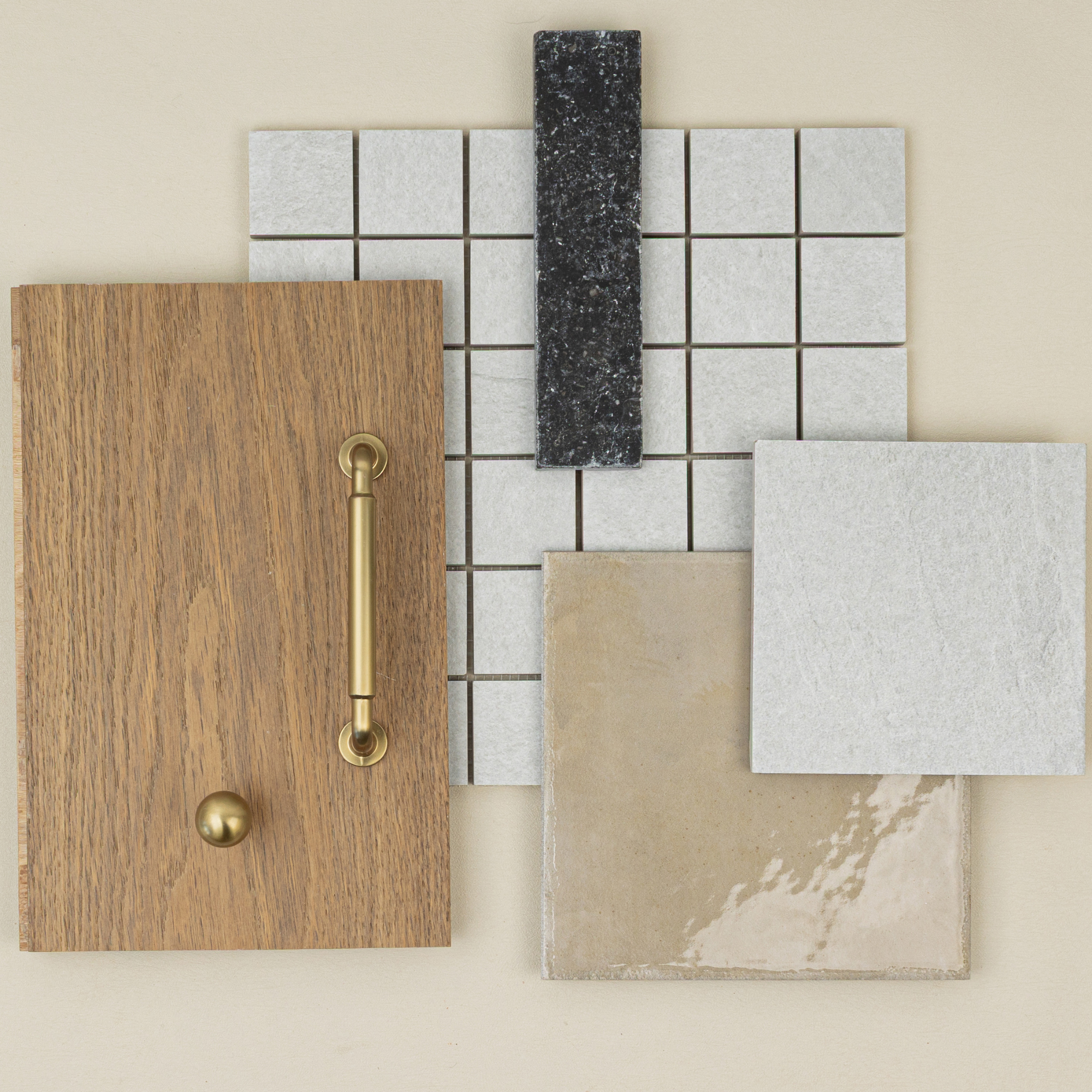 Arrangement of wood sample with brass hardware, light beige and gray tiles, dark slate strip, and square mosaic on neutral background