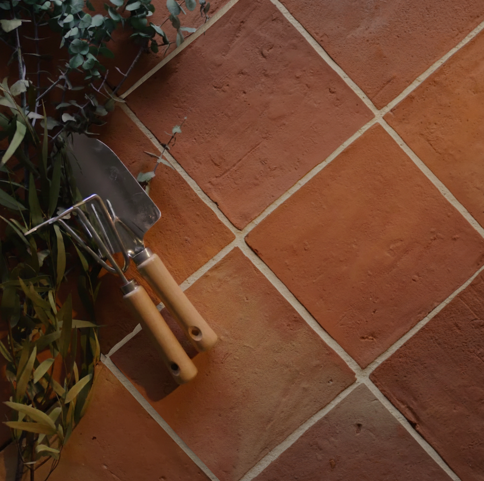 Terracotta-style tiles with natural texture arranged diagonally next to garden tools and leafy branches.